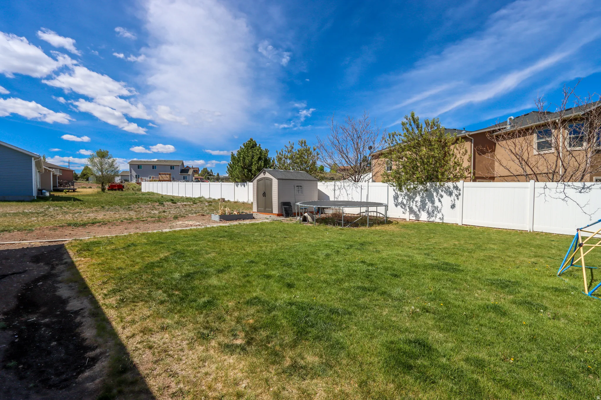 Spacious backyard featuring a large grassy area, white privacy fencing, and a dedicated storage shed