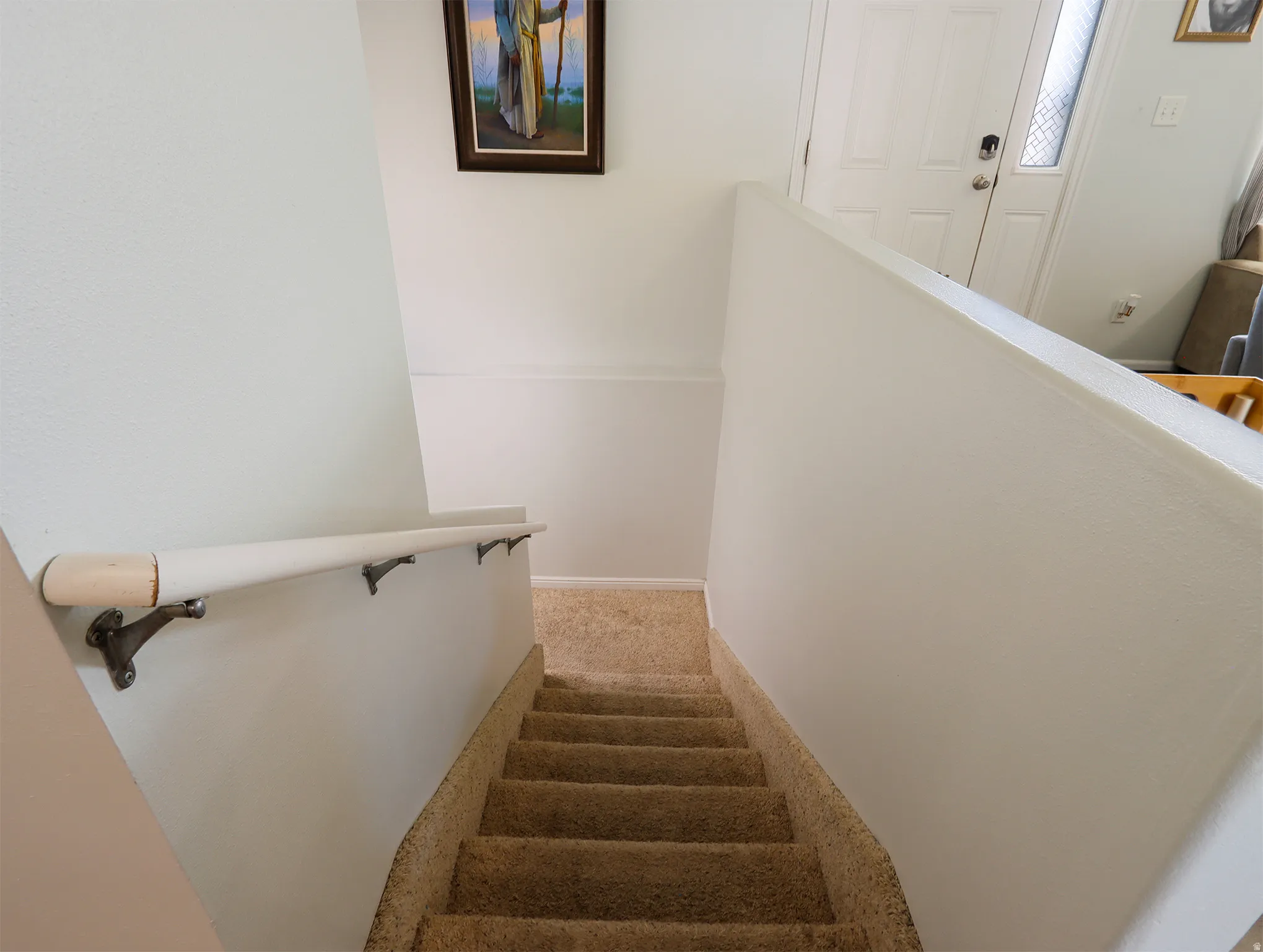 Carpeted staircase with light-colored walls and a wall-mounted handrail