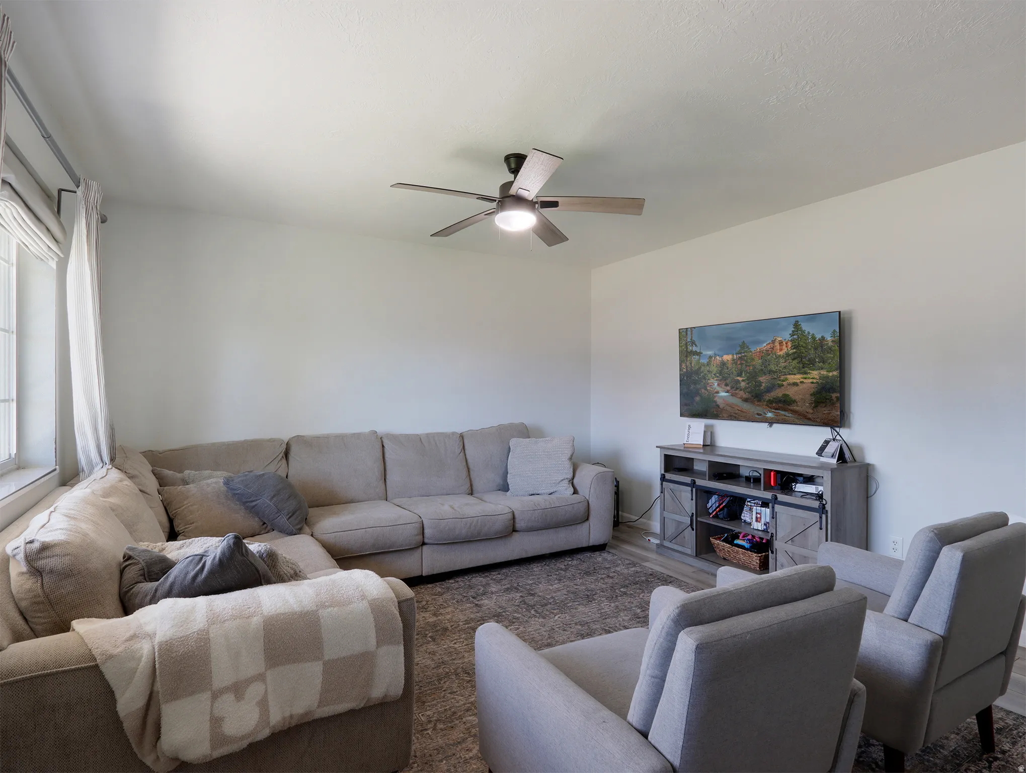 Living area featuring neutral wall tones, a ceiling fan with integrated lighting, and a window with blinds