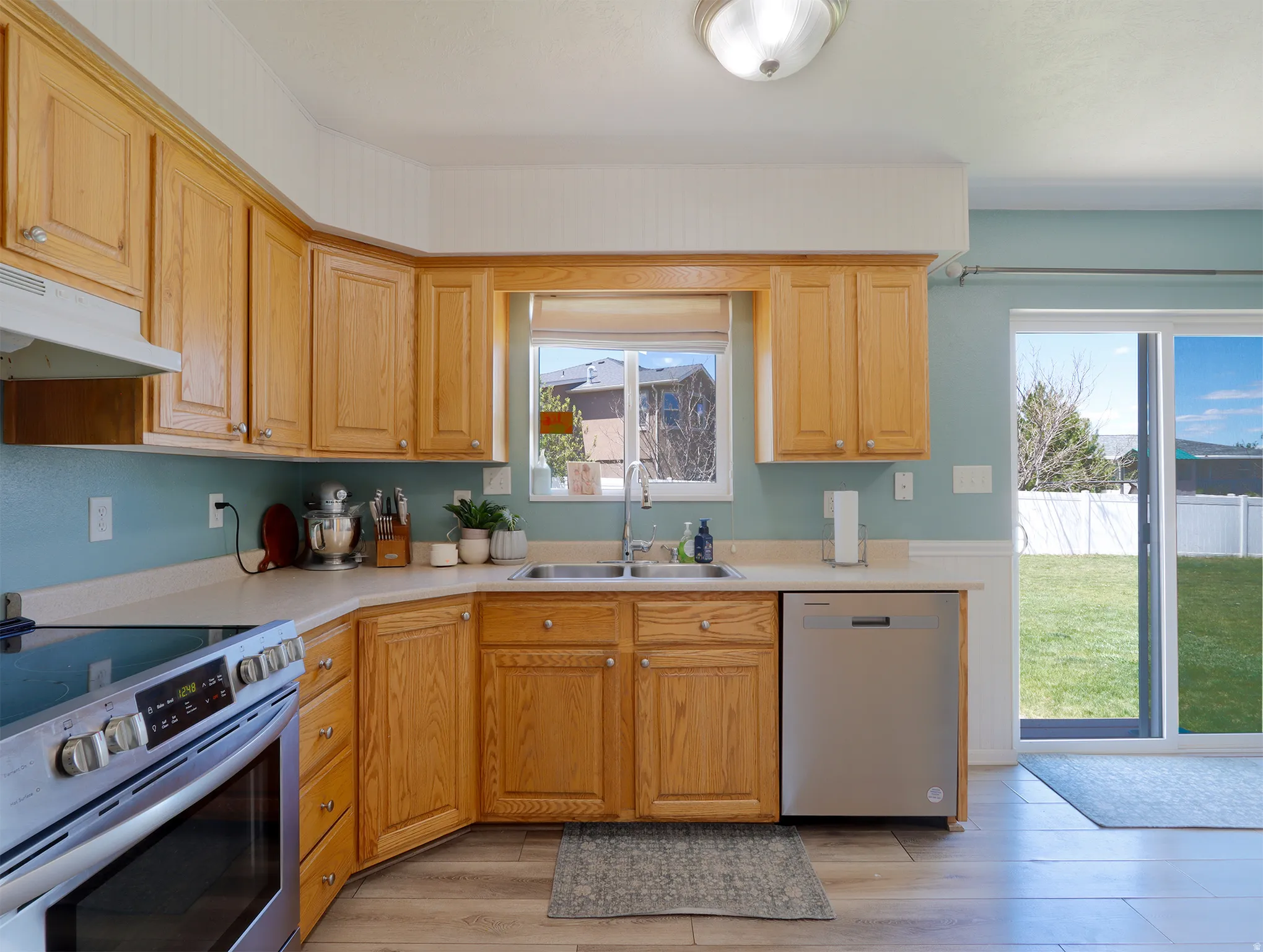 Kitchen featuring wood cabinetry, light countertops, stainless steel appliances, and wood-finish flooring