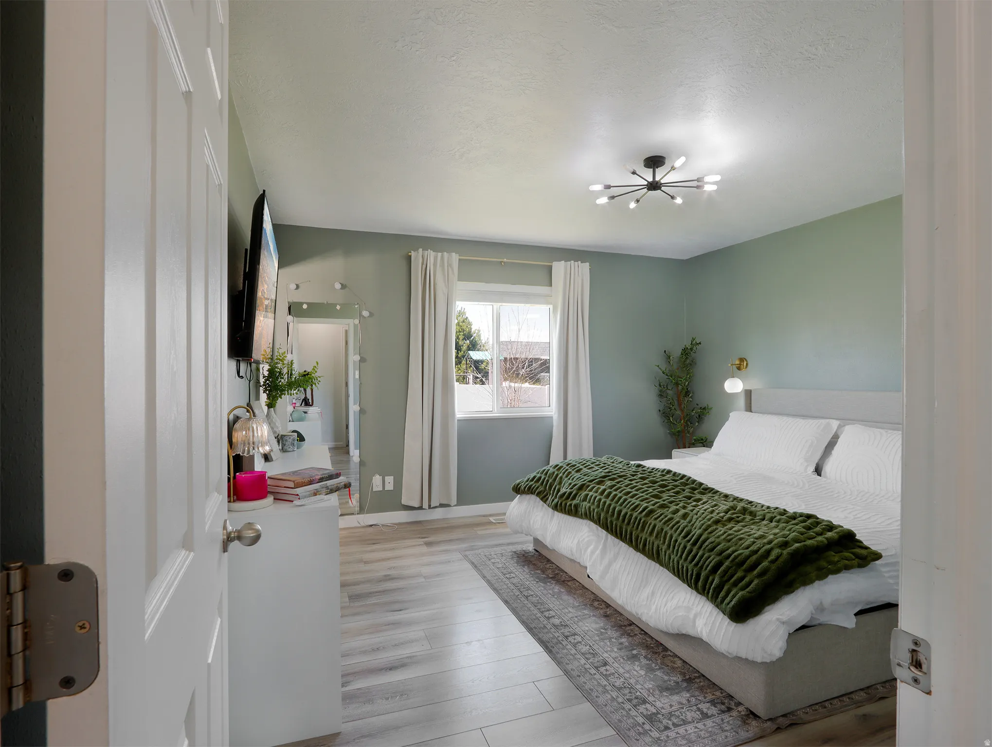 Bedroom featuring light green walls, wood-finish flooring, and a contemporary multi-light ceiling fixture