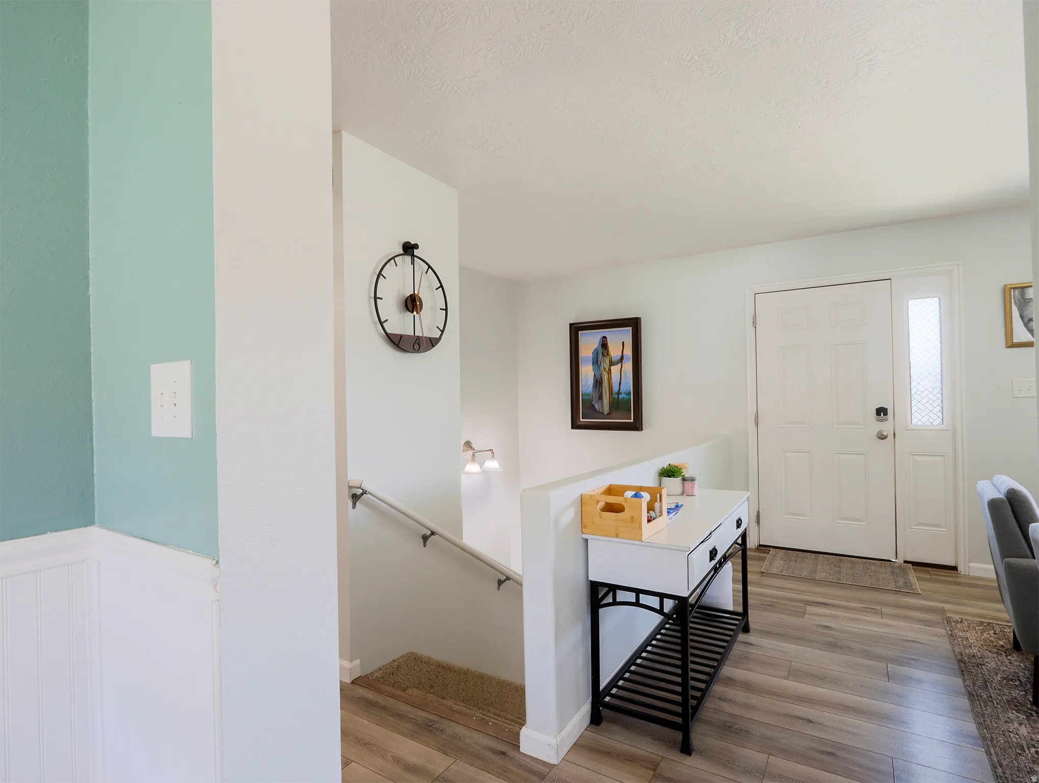 Entryway featuring wood-finish flooring, a white paneled front door with decorative glass sidelite, and a painted staircase with a metal handrail