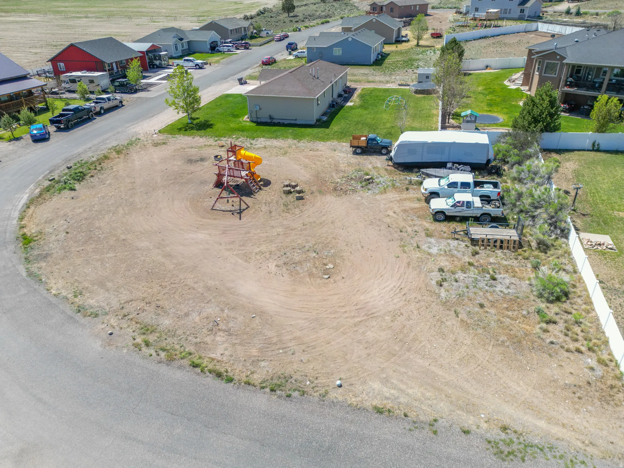 Expansive corner lot featuring a partial paved street frontage and visible residential structures in the background