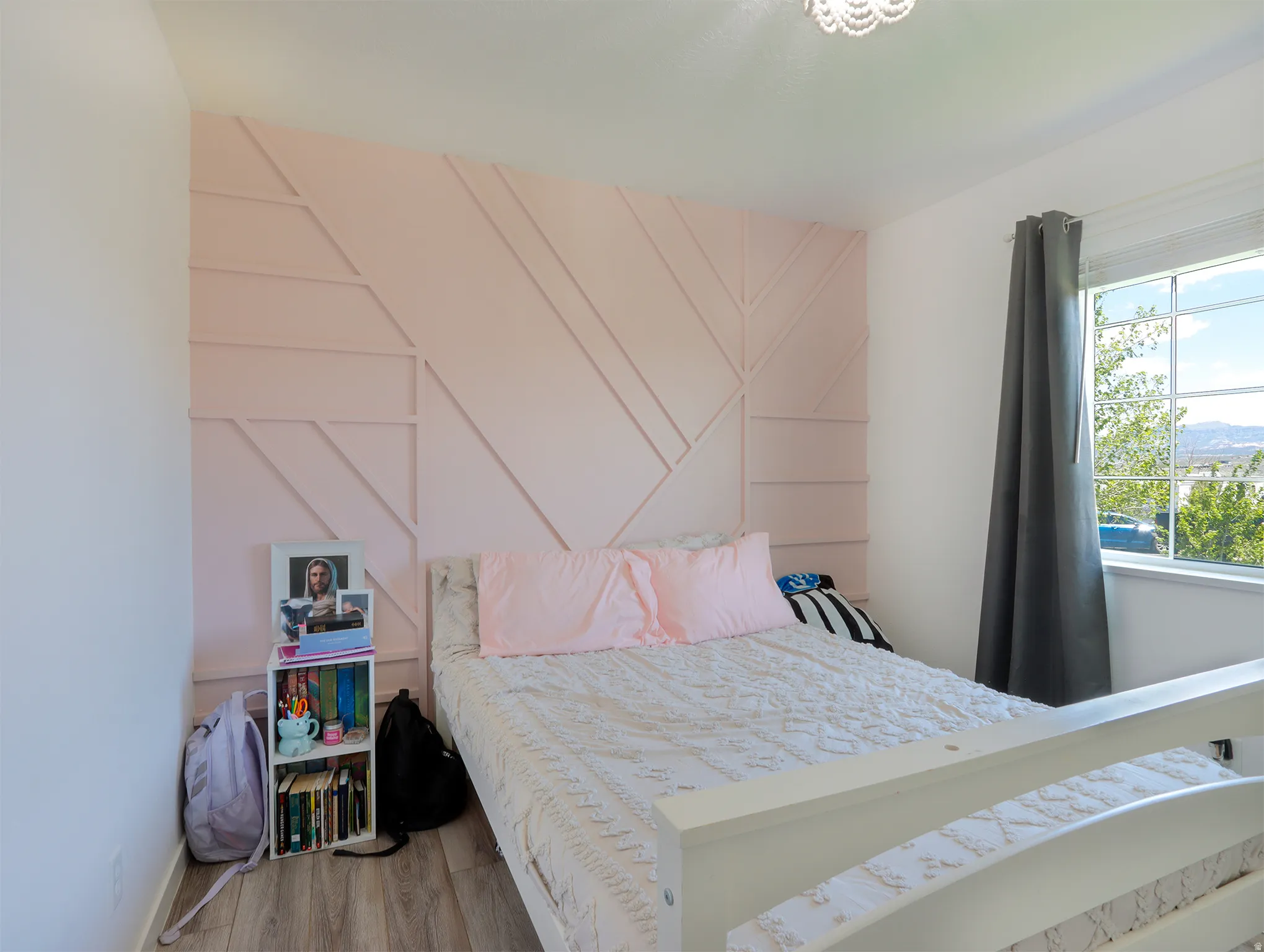 Bedroom featuring a decorative accent wall with geometric molding, natural light from a double-pane window, and wood-finish flooring