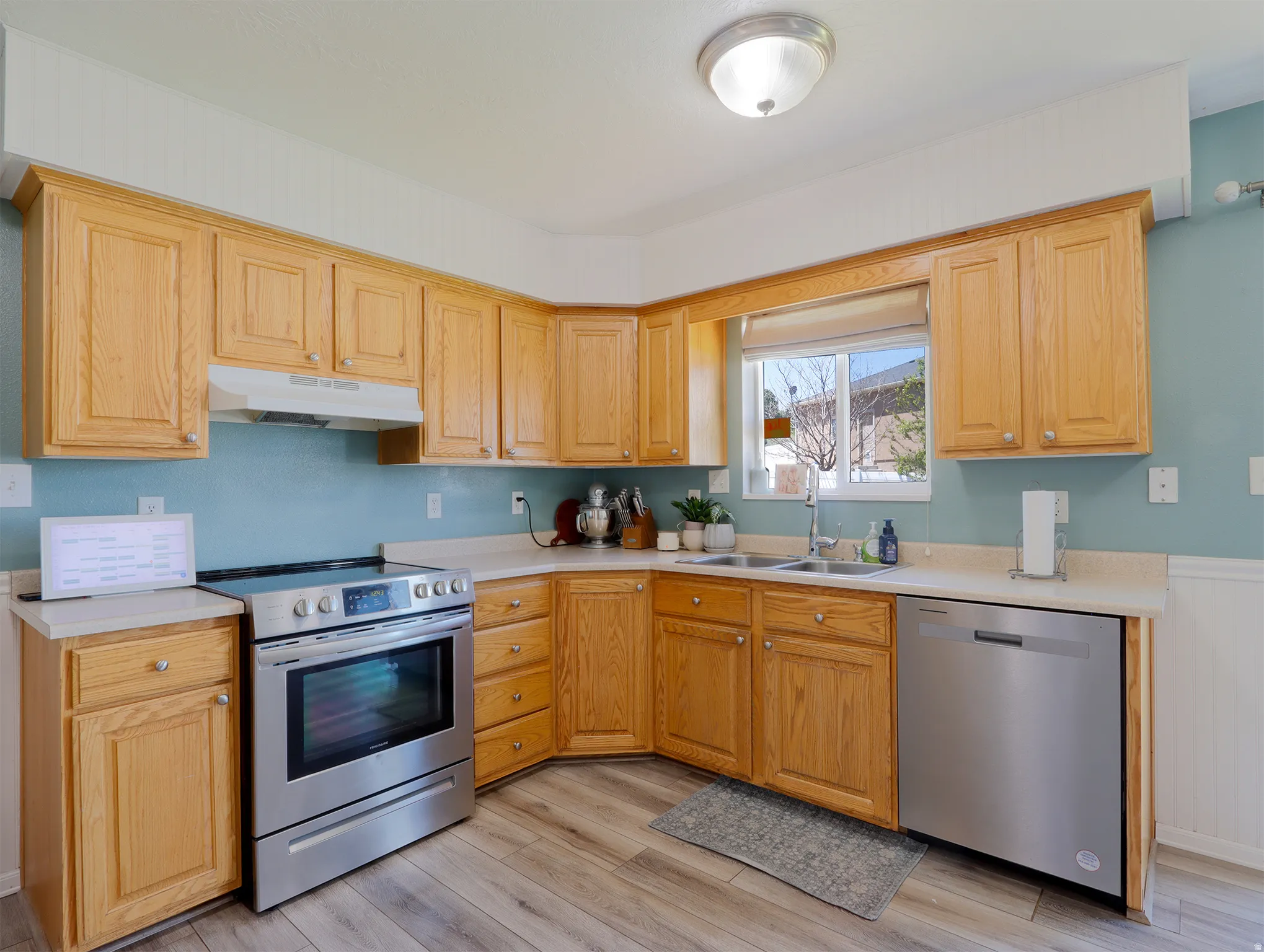 Kitchen featuring wood-finish cabinetry, stainless steel range, stainless steel dishwasher, light-toned countertops, and wood-finish flooring