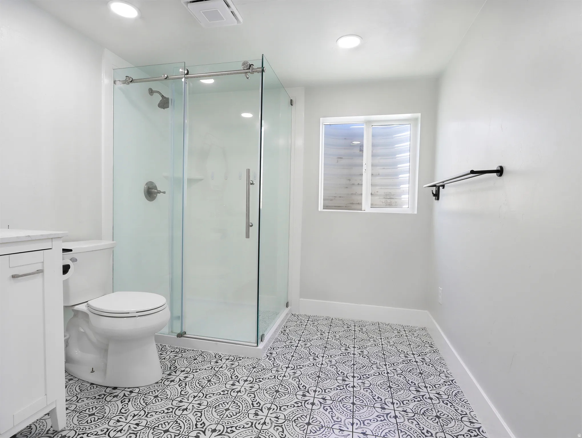 Bathroom featuring a glass-enclosed shower with sliding door, white vanity cabinet, and patterned floor tiles