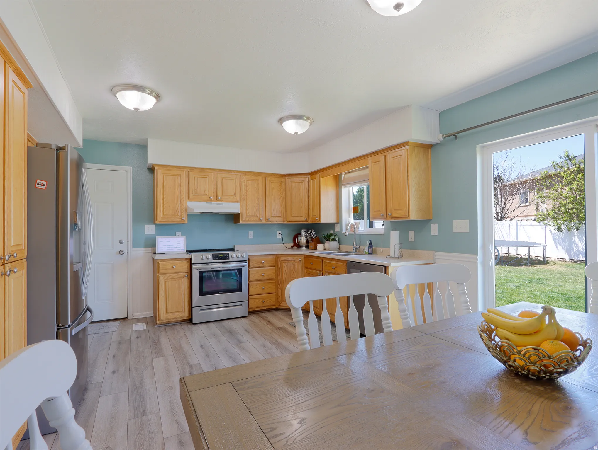 Kitchen featuring natural wood cabinetry, stainless steel appliances, light-toned countertops, wood-finish flooring, and direct access to the outdoor space via sliding glass doors