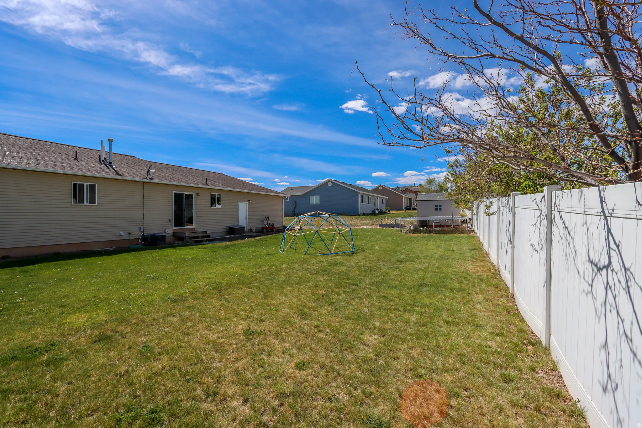 Expansive grassy yard featuring a white privacy fence, a detached shed, and mature trees