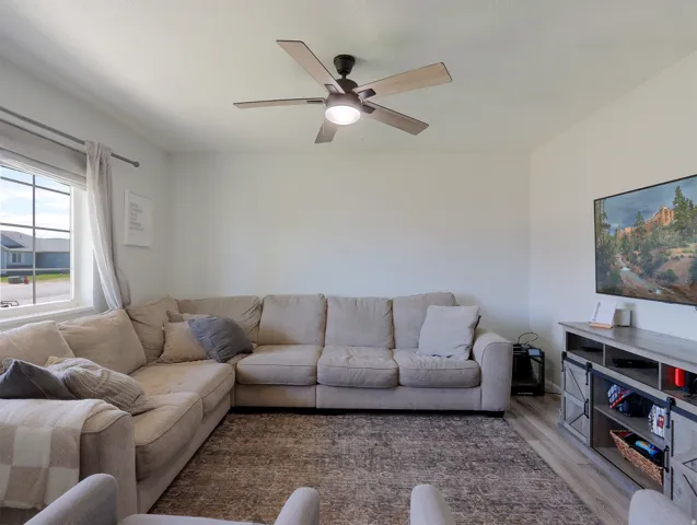 Light-filled living area featuring a ceiling fan, a large window, and wood-finish flooring