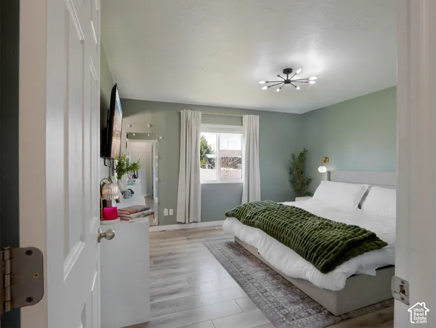 Bedroom featuring light green walls, wood-finish flooring, and a contemporary multi-light ceiling fixture