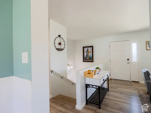 Entryway featuring wood-finish flooring, a white paneled front door with decorative glass sidelite, and a painted staircase with a metal handrail