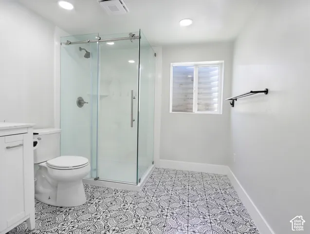 Bathroom featuring a glass-enclosed shower with sliding door, white vanity cabinet, and patterned floor tiles