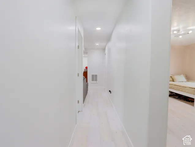 Hallway featuring light-toned wood-finish flooring, recessed lighting, and white walls