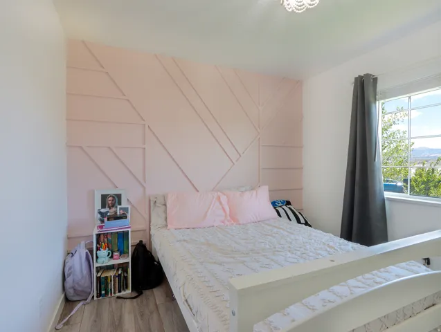Bedroom featuring a decorative accent wall with geometric molding, natural light from a double-pane window, and wood-finish flooring