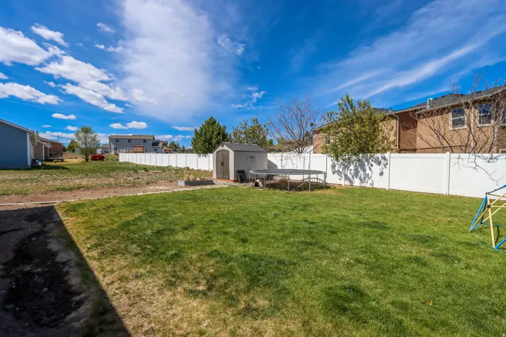 Spacious backyard featuring a large grassy area, white privacy fencing, and a dedicated storage shed