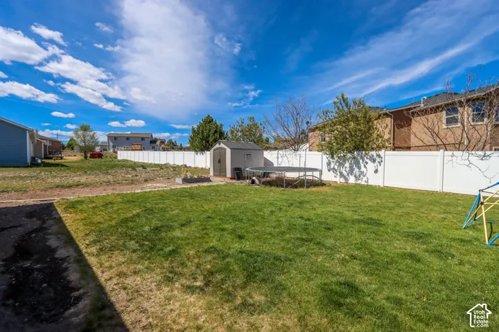 Spacious backyard featuring a large grassy area, white privacy fencing, and a dedicated storage shed