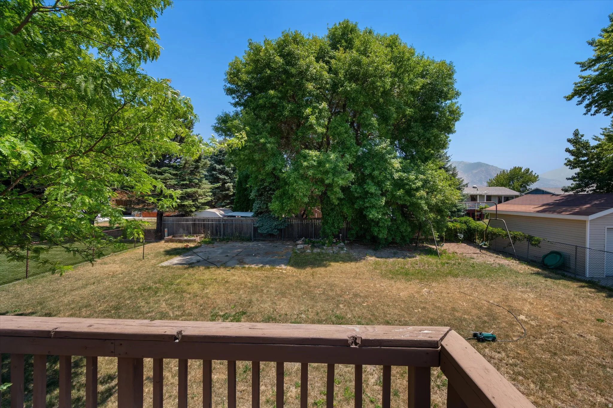 Expansive fenced backyard featuring mature trees, a detached garage with vinyl siding, and a concrete patio area