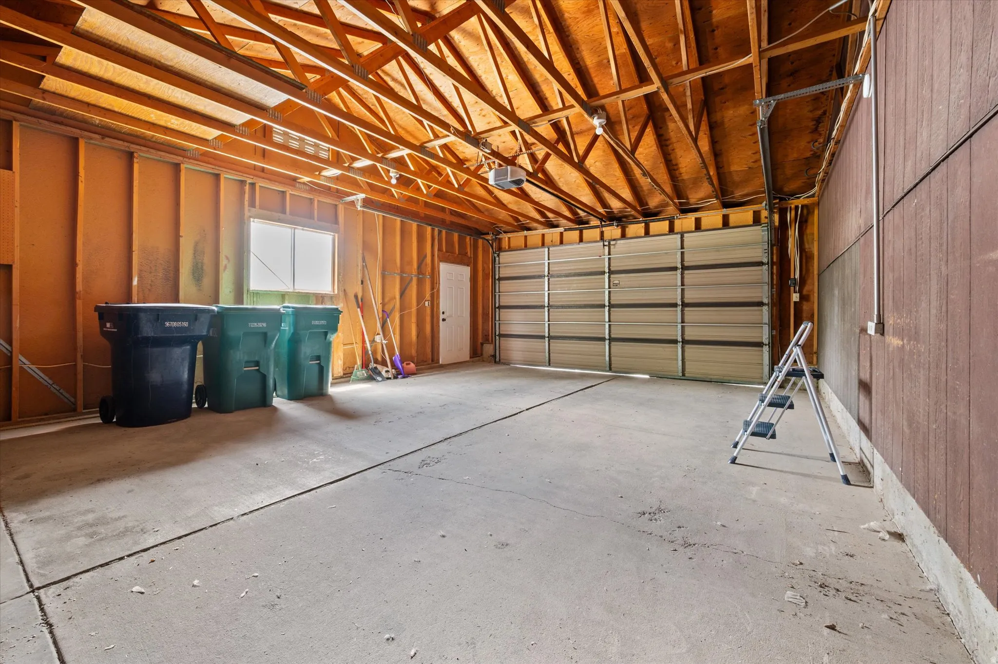 Spacious garage with exposed wood beam ceiling, concrete flooring, and a large sectional garage door