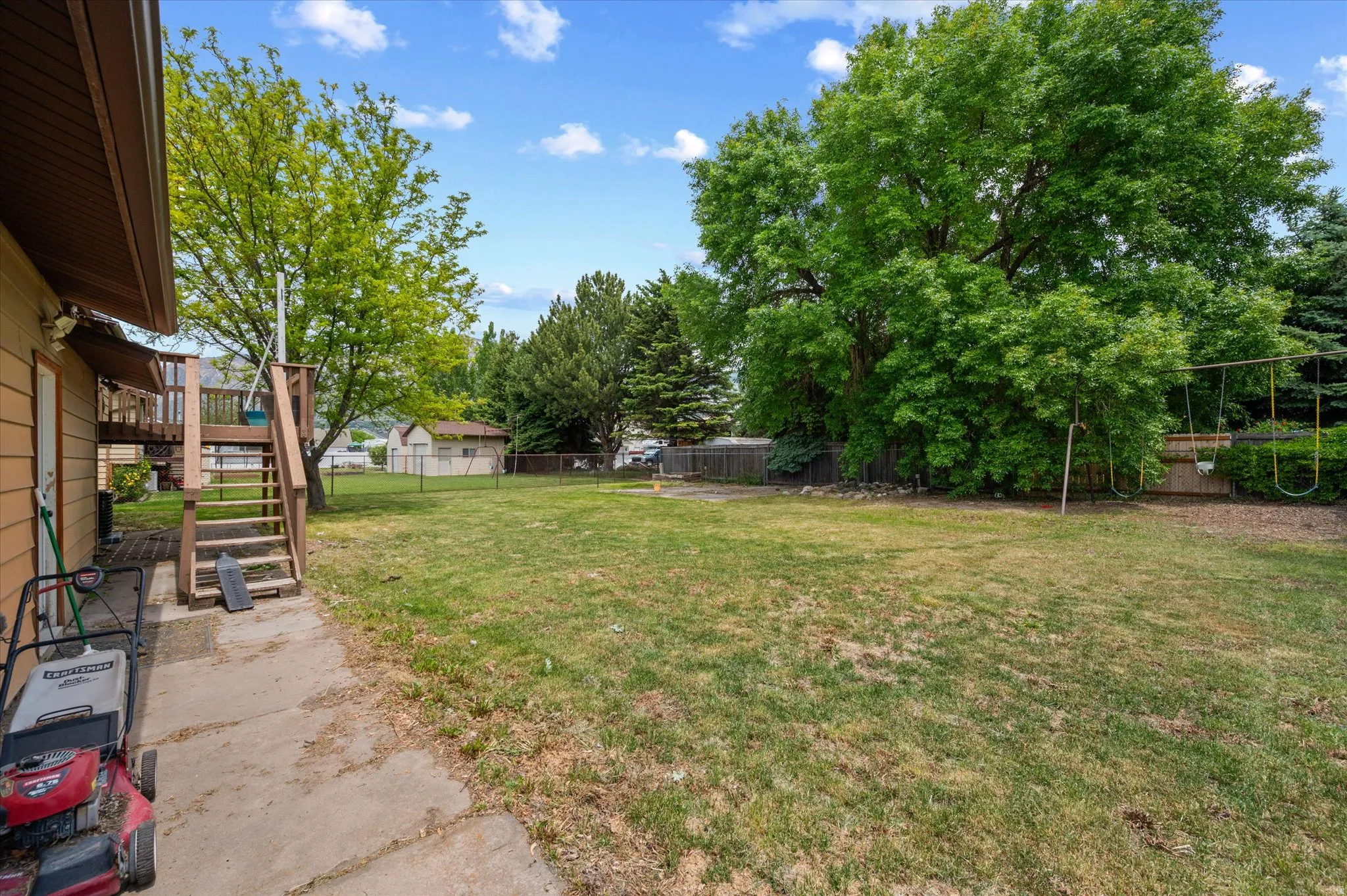 Expansive backyard featuring a large grass lawn, mature trees, and a wooden deck with stairs