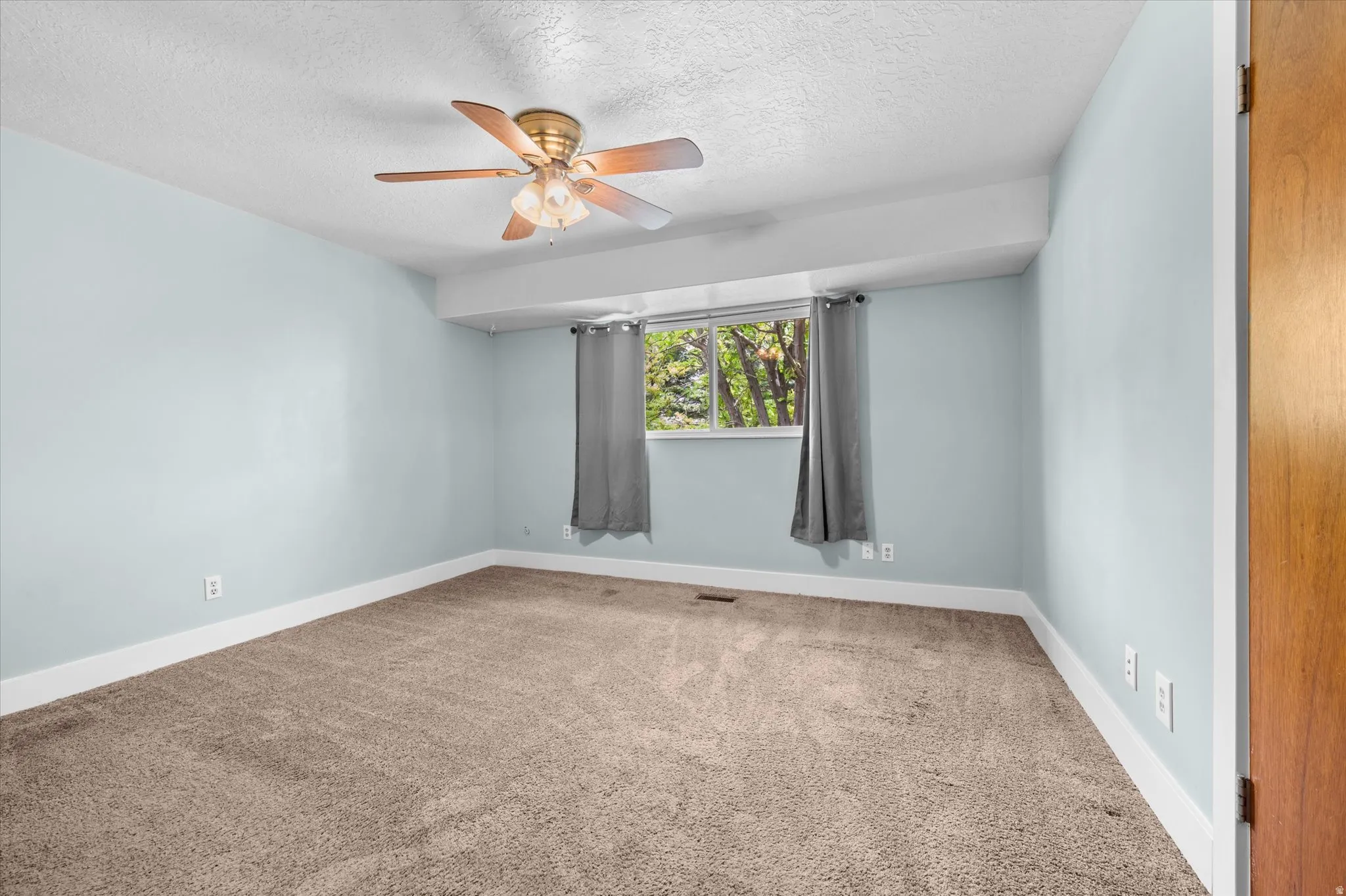 Carpeted Primary bedroom featuring a ceiling fan, a window with exterior tree scenery, and a bathroom entrance door.
