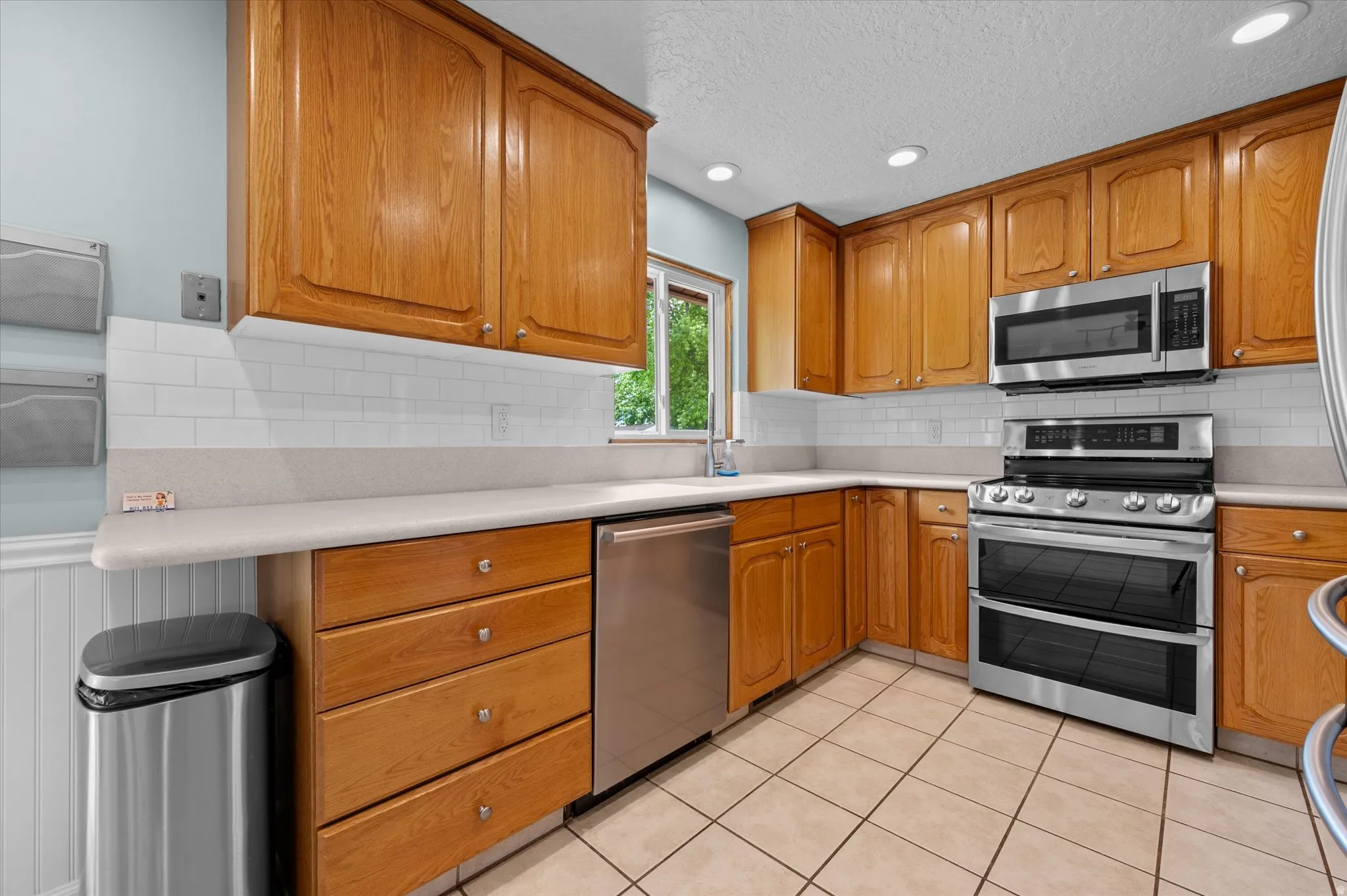 Kitchen featuring natural light, stainless steel appliances, ample light wood cabinetry,  and light-toned countertops