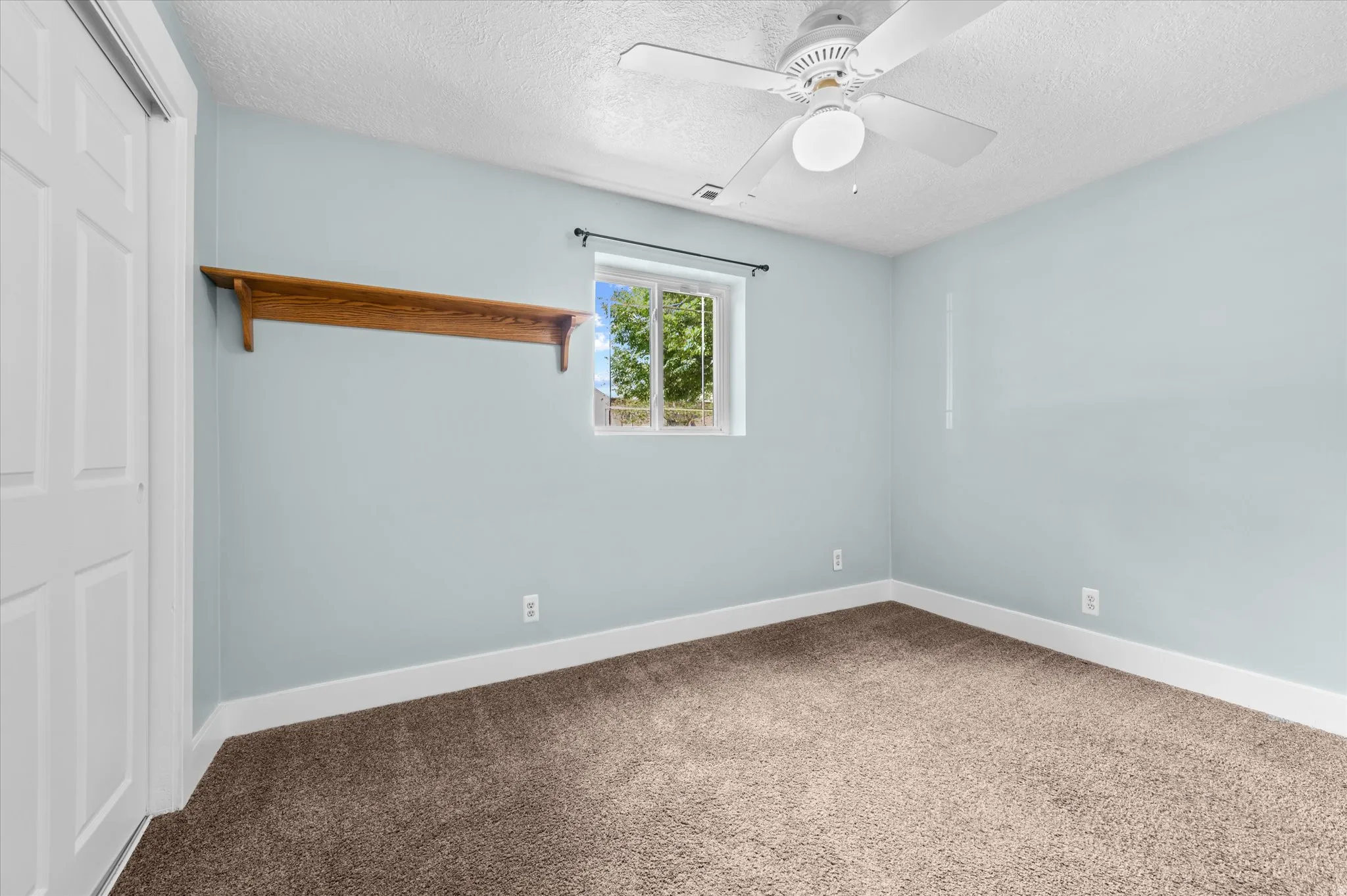 Bedroom #4 with Light blue interior wall, window with exterior landscape, built-in wooden shelf, and a ceiling fan with light fixture