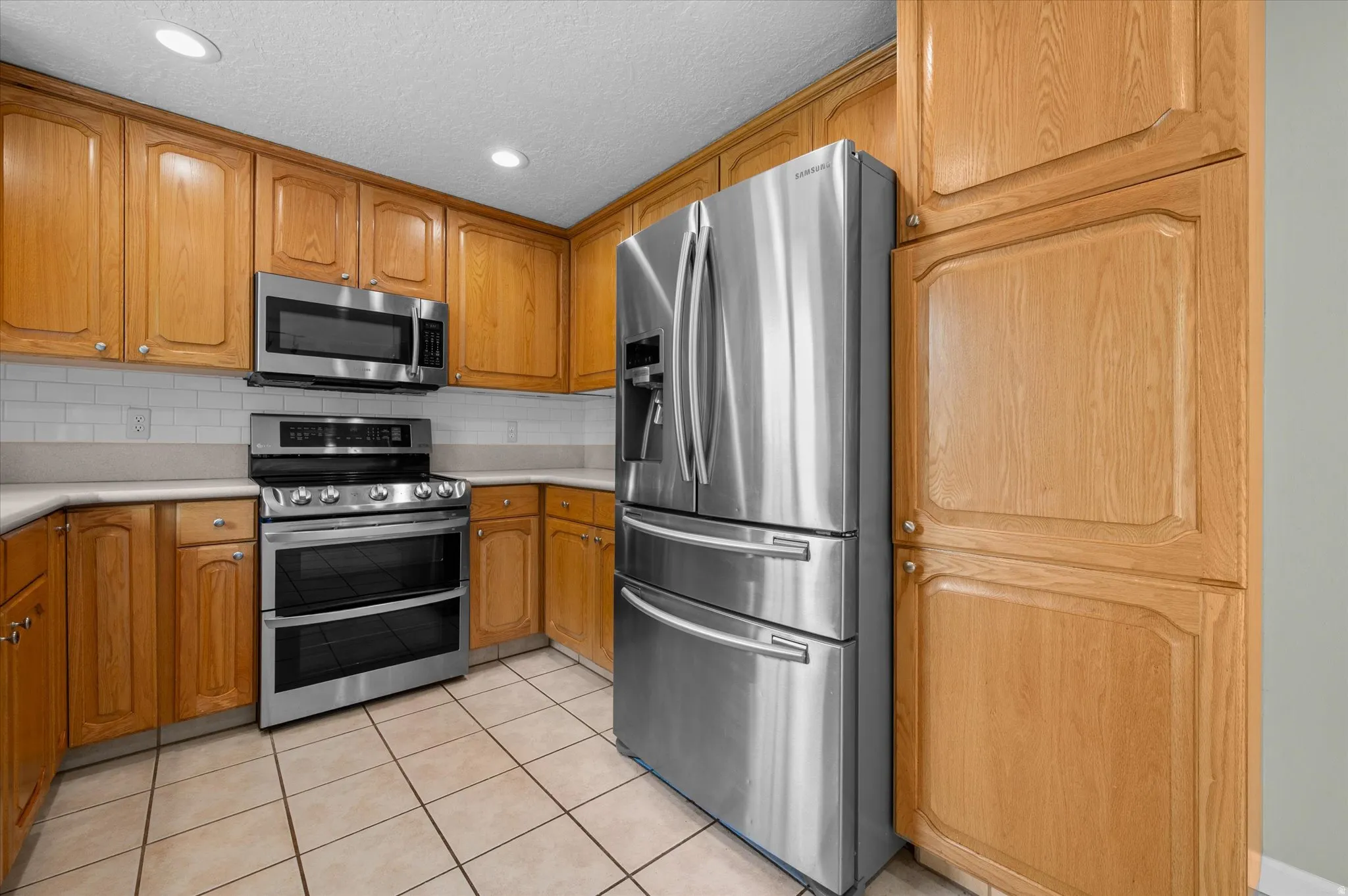 Kitchen featuring ample light wood cabinetry, stainless steel appliances, white subway tile backsplash, and light-toned countertops