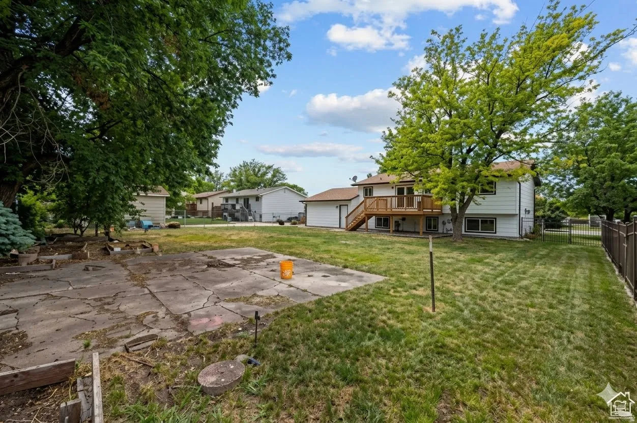 Expansive backyard featuring a large concrete patio, substantial grassy areas, mature trees, and a privacy fence