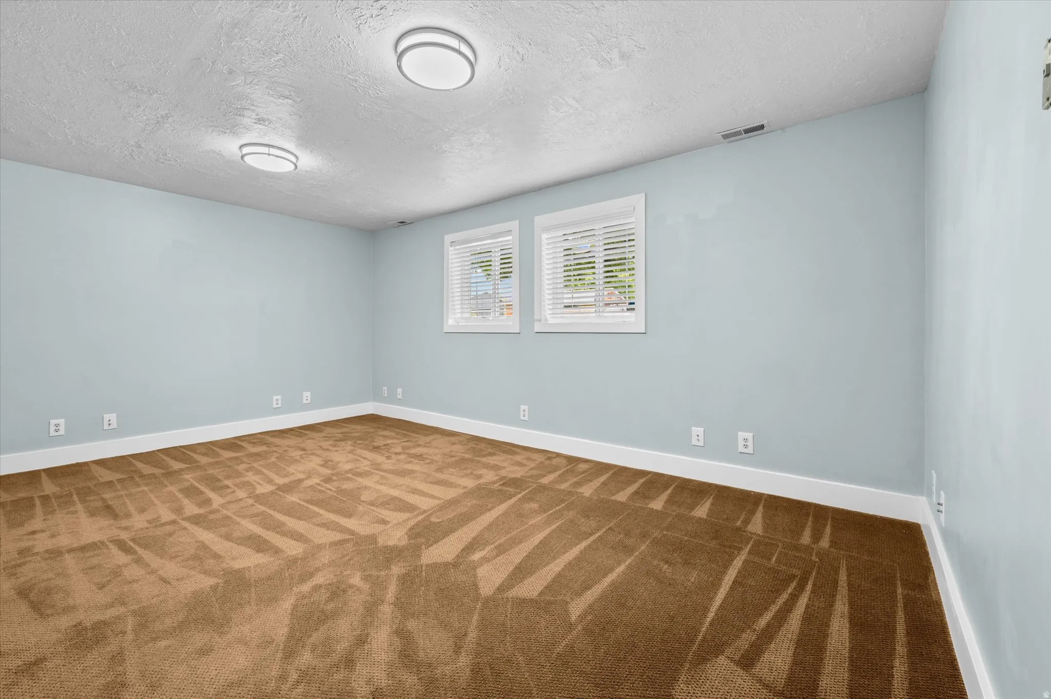 Spacious family room featuring light blue walls and a textured brown carpet