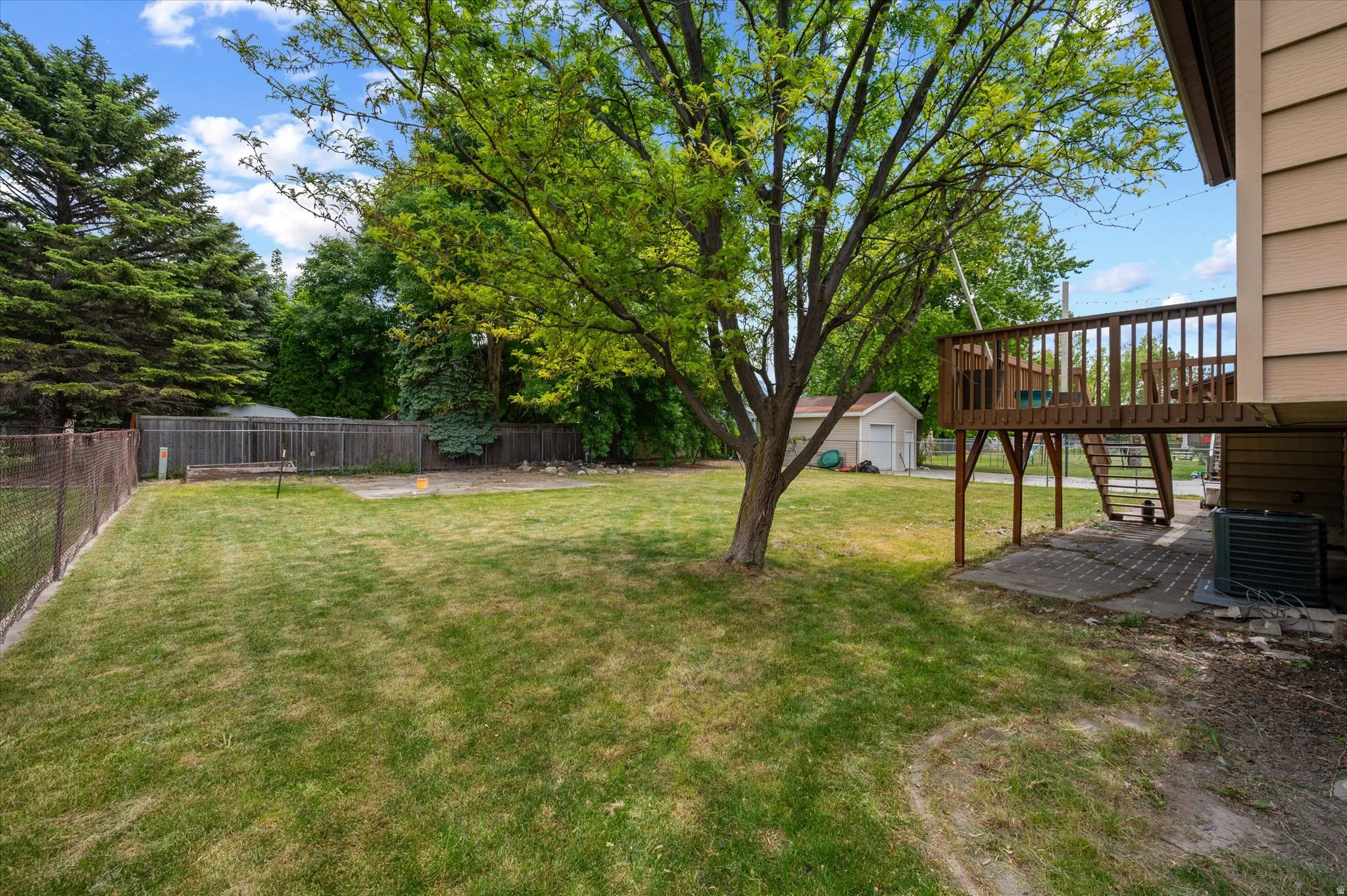 Spacious backyard with a raised wood deck, mature tree, perimeter fencing, 12 x 12 patio, and a raised vegetable garden