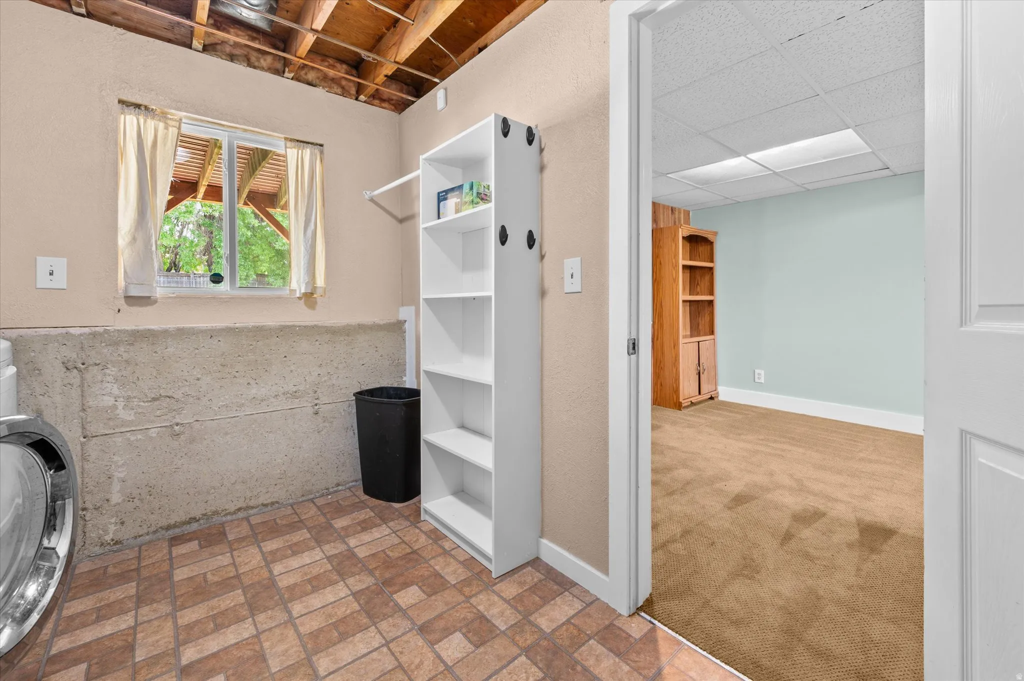 Utility area featuring patterned tile flooring, exposed wood beam ceiling, and a built-in shelving unit