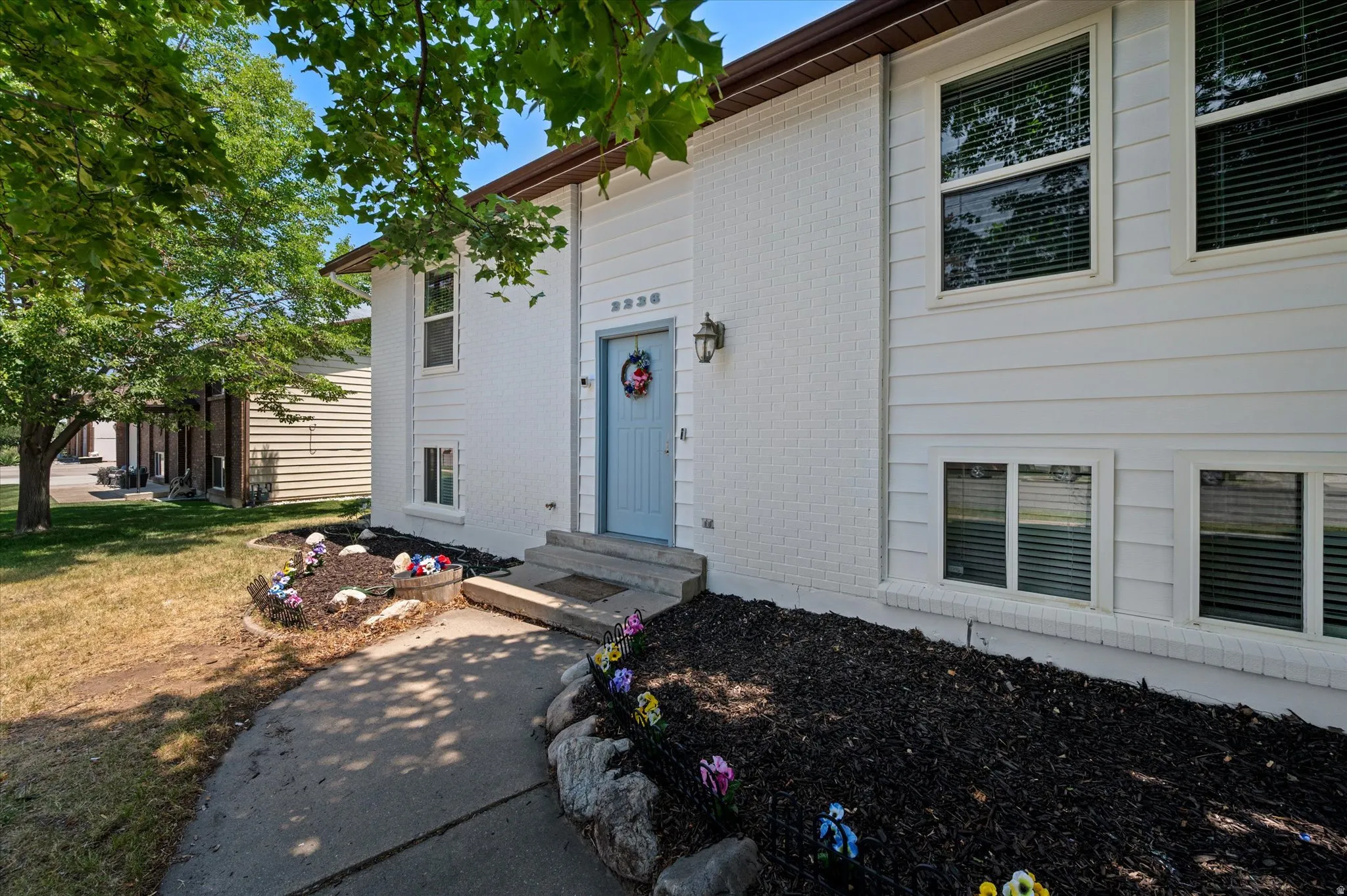 White exterior siding and brick facade, light blue entry door and a garden area