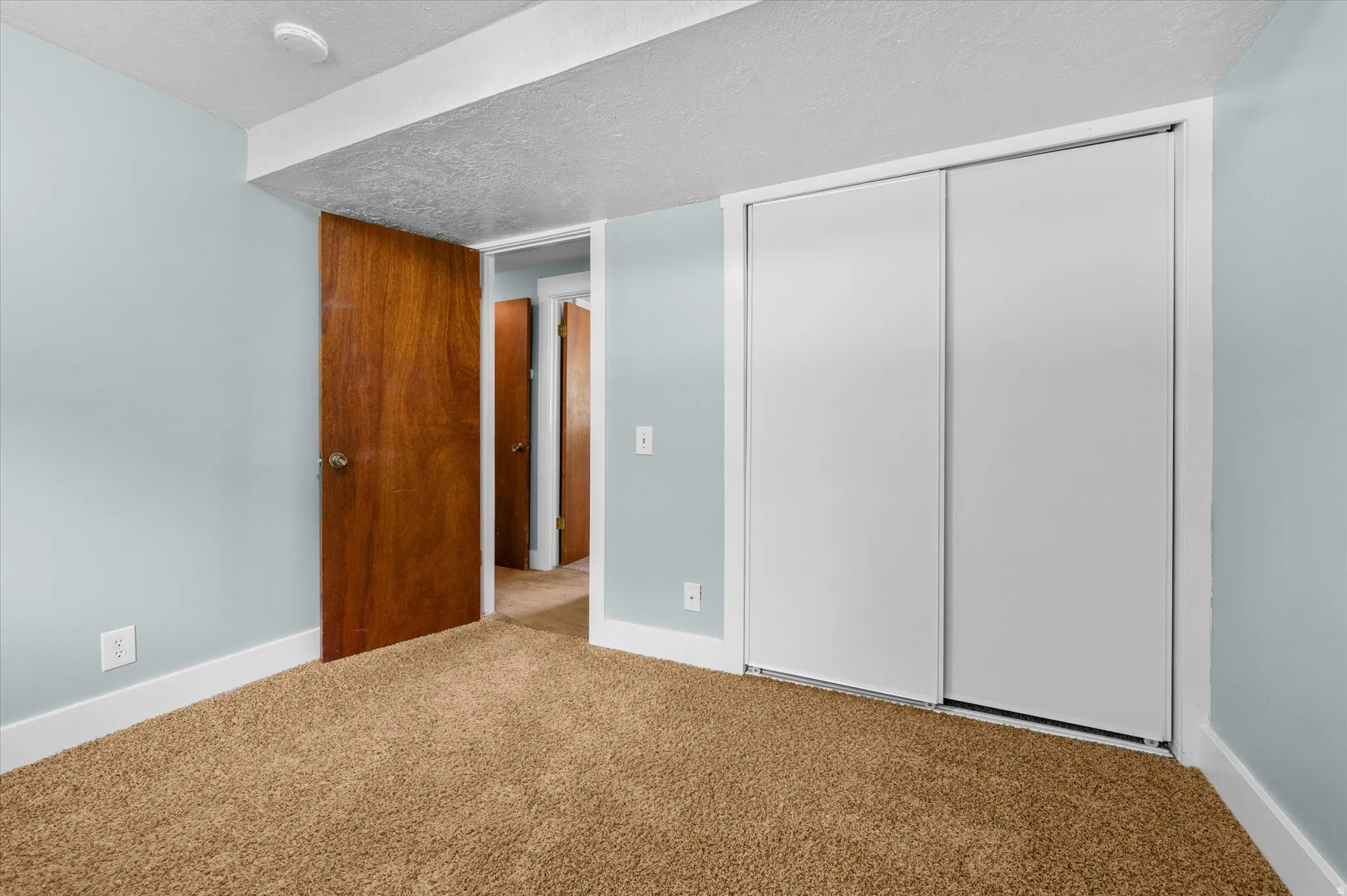 Interior bedroom #3  featuring light blue walls, brown carpet, white baseboards, and a white sliding closet door
