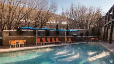 Outdoor swimming pool featuring a stone surround, multiple patio umbrellas, and various lounge seating options