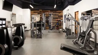 Fitness center featuring a variety of exercise equipment, wood accent wall, mirrored wall, wall-mounted television, and overhead lighting