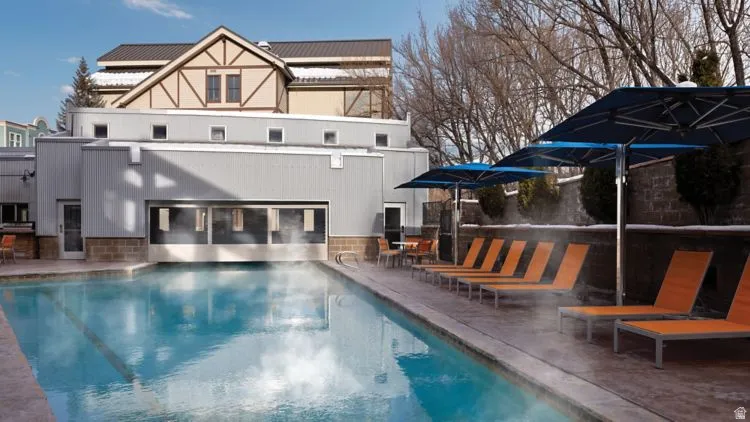 Outdoor swimming pool with concrete decking, surrounded by lounge chairs and blue patio umbrellas