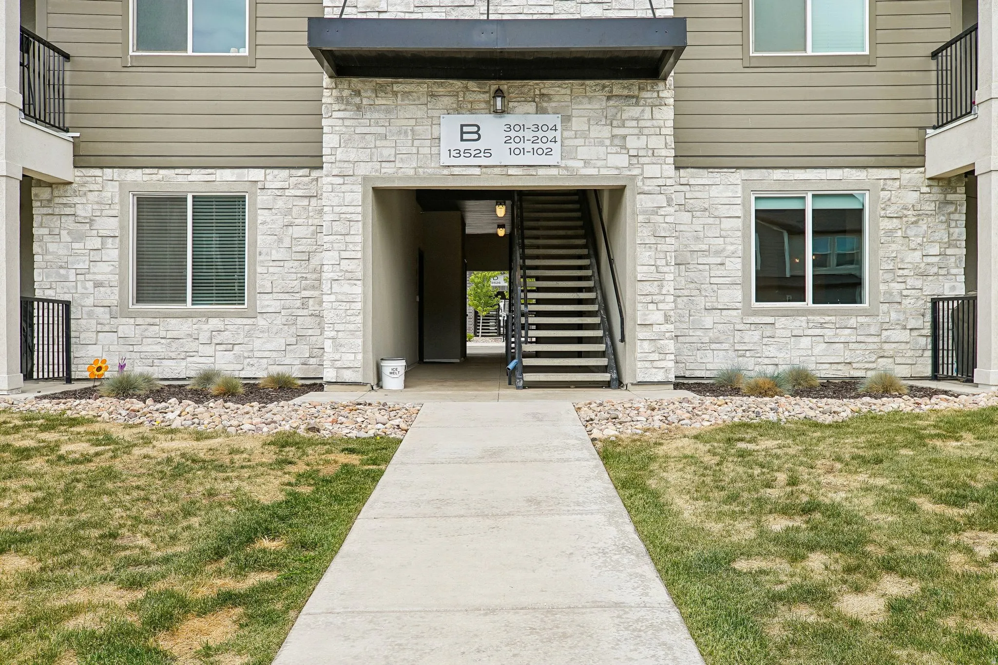 Multi-level building exterior featuring a concrete walkway, stone veneer siding, horizontal paneling, and an exposed metal staircase with railing