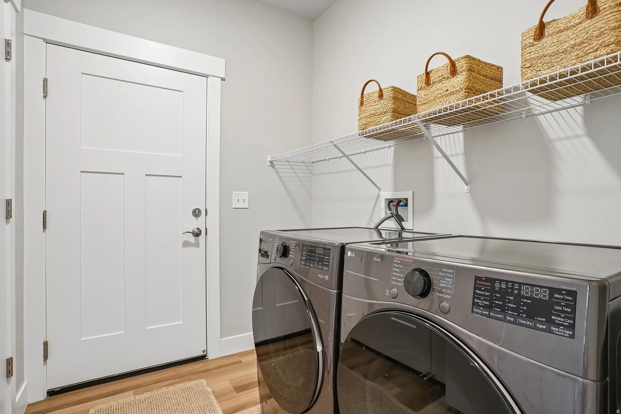 Laundry area featuring wood-finish flooring, a white three-panel door with white trim, and a built-in wire shelving unit