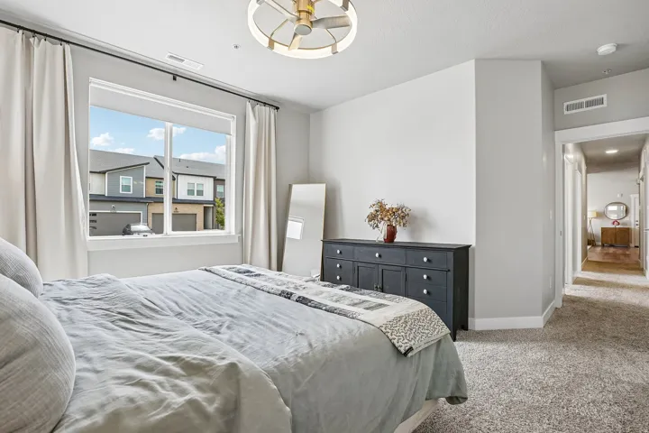 Bedroom featuring a large window with white trim, light-colored walls, and a modern ceiling fan with gold accents
