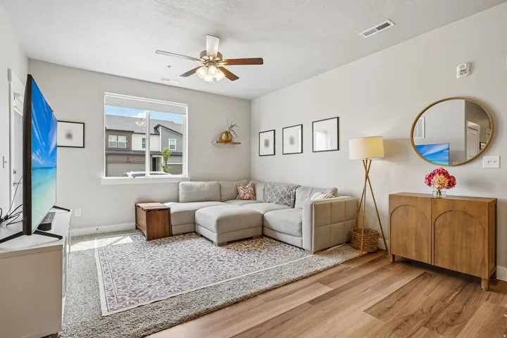 Bright living area featuring wood-finish flooring, a large window, a ceiling fan with integrated lighting, and neutral wall tones