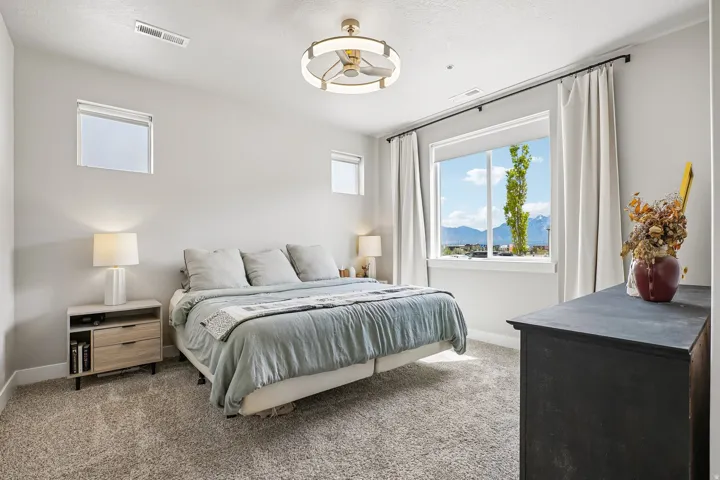 Carpeted bedroom featuring a large window with mountain scenery, two transom windows, a ceiling fan with integrated lighting, and light gray wall paint