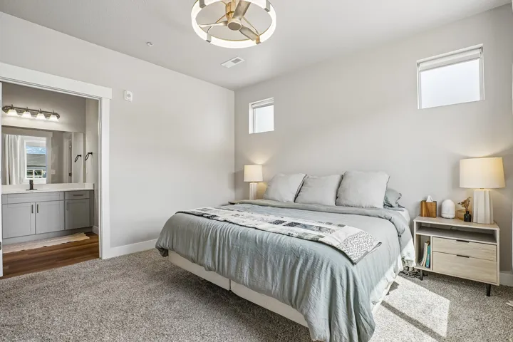 Carpeted room featuring a contemporary ceiling fan, multiple windows, and a doorway opening to a bathroom