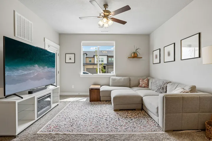 Living area featuring light-toned walls, a ceiling fan with integrated lighting, and carpeted flooring