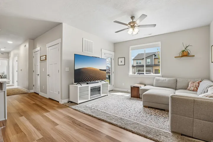 Open-concept living area featuring wood-finish flooring, a ceiling fan with integrated lighting, and a large window providing ample natural light
