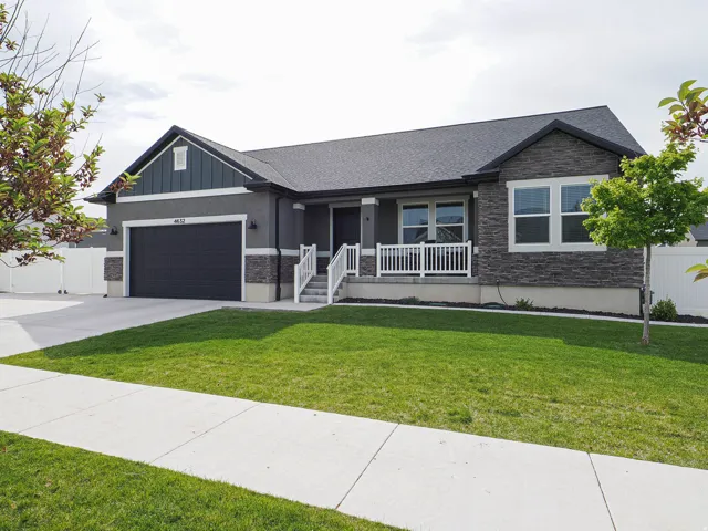 Contemporary ranch-style residence featuring a dark gray exterior, prominent stone accents, an attached two-car garage, white porch railings, and a meticulously maintained front lawn