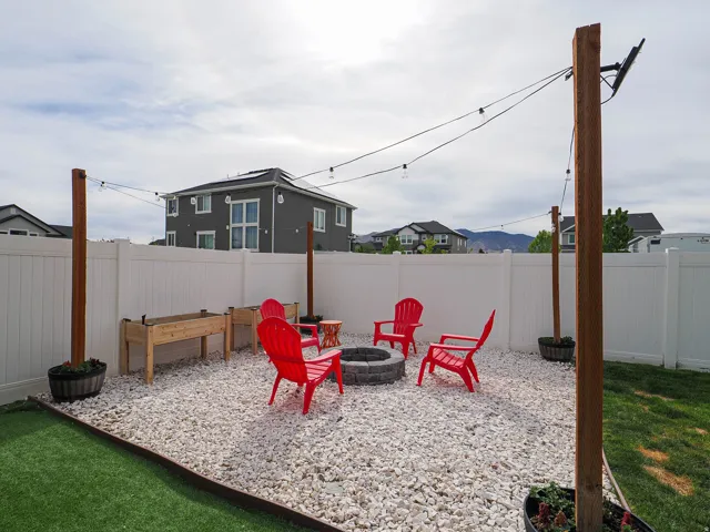Private backyard featuring a white vinyl fence, string lights, and a stone fire pit area with white decorative rock