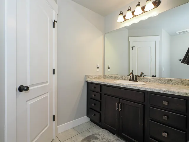 Bathroom vanity featuring a light-toned countertop, dark wood-finish cabinetry, and a single undermount sink with a bronze-toned faucet
