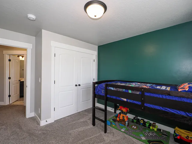 Carpeted room featuring a white paneled bi-fold closet door, a flush-mount ceiling light fixture, a smoke detector, and a painted accent wall