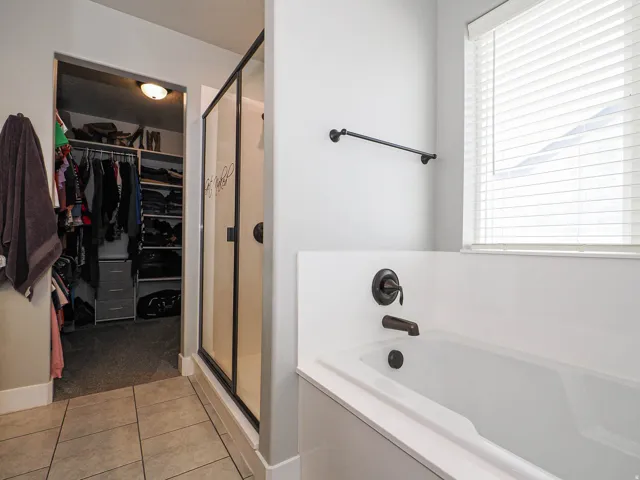 Bathroom featuring a built-in tub, separate glass-enclosed shower, dark bronze fixtures, and tile flooring