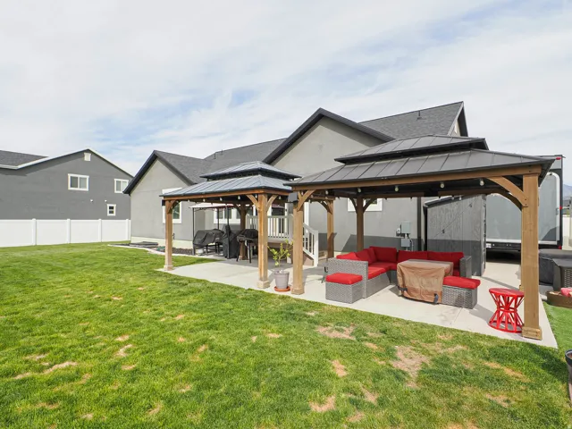 Expansive backyard featuring a large concrete patio, two permanent pergolas with string lighting, a wooden deck, and a full white vinyl fence